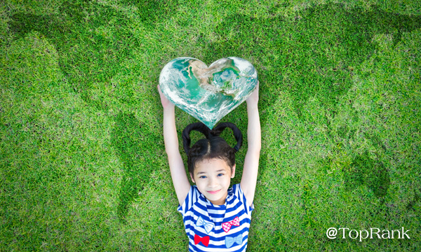Smiling girl on lawn holding a heart-shaped earth image.